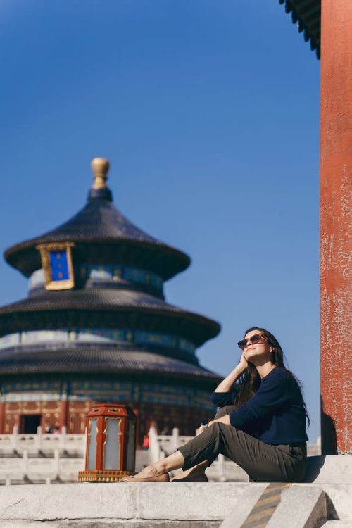 Mujer sonriente con gafas de sol sentada frente al Templo del Cielo en Pekín