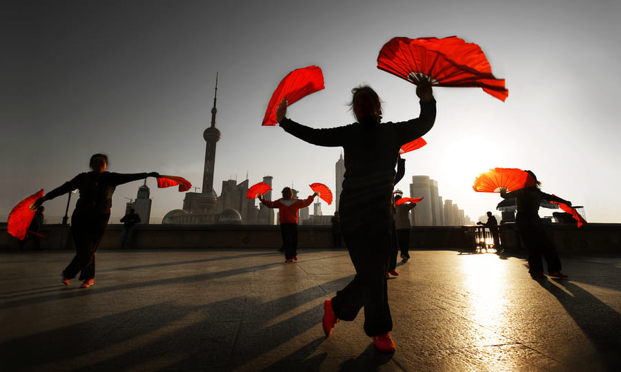 Bailarines con abanicos rojos en el Bund de Shanghái al amanecer o al atardecer.