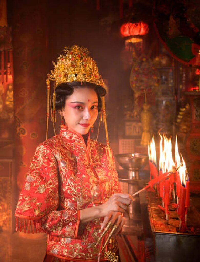 Mujer china con vestimenta tradicional en un templo, junto a un león de danza y velas